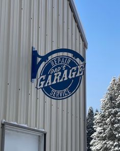 a sign on the side of a building that says repair garage service in front of snow covered trees