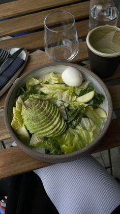 a bowl filled with lettuce and an egg on top of a wooden table