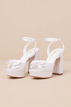 Your walk down the aisle just got even more fabulous, thanks to the Lulus Pearlla Bow White Satin Platform High Heel Sandals! These sleek satin heels feature a trendy square toe upper (atop a 1"" toe platform), and a wide toe strap adorned with a darling bow detail. Matching straps sprout from the sides to wrap and secure around the ankle with a gold buckle, all atop a sky-high block heel that is sure to take your look to the next level! 4. 5" wrapped block heel. Cushioned insole. Felted rubber White High Heels For Quinceanera, White Wedges Heels, White Shoes With Bow, Confirmation Heels, White Heels Simple, High Heels For Graduation, Summer Wedding Satin Shoes, High Heel Satin Sandals For Wedding, Satin Heels With Padded Heel For Wedding