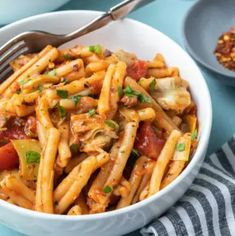 a white bowl filled with pasta and meat on top of a blue table next to a fork