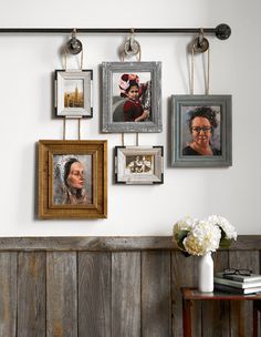 there are many pictures hanging on the wall with hooks and frames above them, along with a vase full of flowers