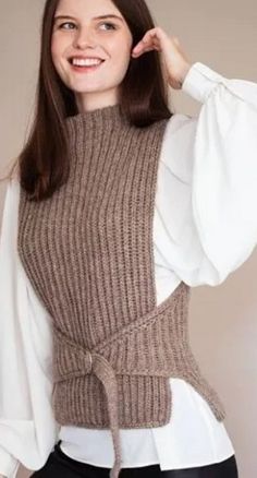 a woman wearing a sweater and black pants posing for the camera with her hands on her hips