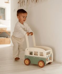 a small child pushing a toy car on the floor in front of a white wall