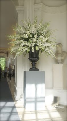 a large vase with white flowers on display in a room filled with statues and windows