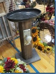 a bird bath sitting on top of a wooden stand next to sunflowers and other flowers