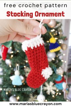 a hand is holding a stocking ornament in front of a christmas tree