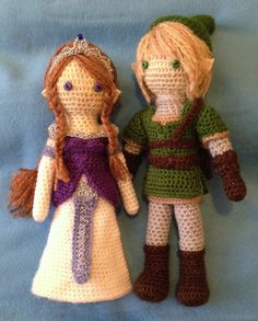 two crocheted dolls sitting next to each other on a blue surface, one wearing a green and purple dress