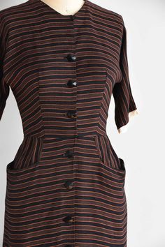 "Vintage 1950s cotton fitted dress. Vertical black and orange stripes. High collar, longer capped sleeves, seamed bust and nipped waist. Straight skirt with front pockets. Stream of front buttons for closure. State of garment | excellent Measurements ✂--- best fit | small bust | 35\" shoulders | not specified shoulder to waist | 15.5\" sleeves | not specified waist | 25-26\" hips | up to 39\" total length (shoulder to hem) | 39 \" ★★Visit The Shop★★ http://www.etsy.com/shop/seaofvintage ➸ Find t Classic Striped Cotton Dress, Fitted Short Sleeve Dress With Striped Collar, Short Sleeve Dresses With Vertical Stripes For Work, Fitted Dresses With Vertical Stripes For Work, Retro Fitted Dress With Vertical Stripes, Fitted Retro Dresses With Vertical Stripes, Classic Striped Dresses For Daywear, Retro Striped Lined Dress, Striped Fitted Dress With Buttons