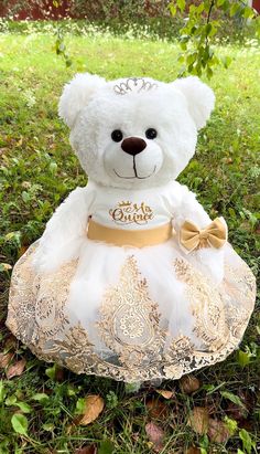 a white teddy bear wearing a dress and tiara sitting on the ground in grass