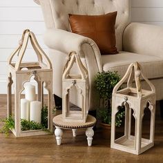 three white lanterns sitting on top of a wooden floor next to a chair and pillow