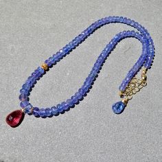 This adjustable necklace features high quality tanzanite gemstones, a deep pink tourmaline drop and 18K yellow gold beads. The sparkling and transparent tanzanite gems are faceted rondelles, graduated in size from 5mm to 7mm. There is a center deep pink tourmaline briolette hand wired with 14K gold wire to the tanzanite strand and the gems are accented with 18K gold beads.  The necklace is adjustable at the back with a gold filled lobster and gold filled chain from 16" to 18" in length. A really Tanzanite Briolette Necklace Gift, Tanzanite Briolette Gemstone Necklace, Briolette Tanzanite Necklace For Gift, Tanzanite Necklace, Tanzanite Gemstone, Tourmaline Necklace, Deep Pink, Oct 31, Gold Wire