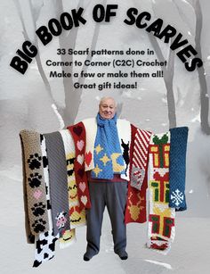 a man standing in the snow holding up some knitted sweaters and scarves