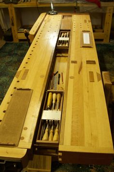 an open drawer on top of a wooden table with tools in it and some other items inside