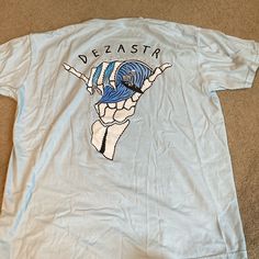 Baby Blue Surfing Skeleton Graph Tshirt. Brand Is Dezster. Size Xlarge. Never Worn. Perfect Condition. Blue Cotton T-shirt With Back Print, Blue Band Merch T-shirt, Blue Crew Neck Shirt With Front Print, Blue Band Merch T-shirt With Graphic Print, Blue Fan Merchandise T-shirt For Summer, Blue Graphic Tee With Back Print, Blue Shirt With Screen Print For Fan Merchandise, Blue Summer Fan Merchandise T-shirt, Blue Crew Neck T-shirt With Back Print