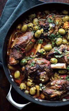 a pot filled with meat and olives on top of a wooden table