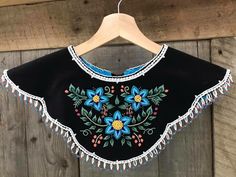 a black top with blue flowers and tassels hanging on a wooden wall