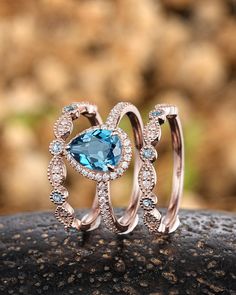 two wedding rings with blue topaz and white diamonds on a rock in front of some rocks