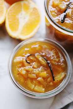 two glass jars filled with food sitting on top of a table next to sliced oranges