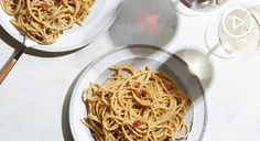 two plates of spaghetti on a table next to wine glasses