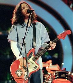 a man with long hair playing an electric guitar in front of a microphone on stage