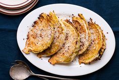 four cooked artichokes on a white plate with silverware next to it