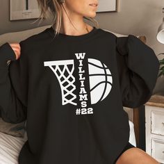 a woman sitting on top of a bed wearing a black shirt with white letters and a basketball