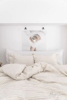 a white bed topped with lots of pillows next to a painting on the headboard