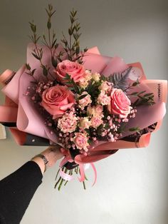 a bouquet of pink roses and greenery is held by a woman's hand