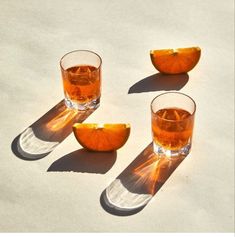 three glasses filled with orange slices sitting on top of a sandy beach next to each other