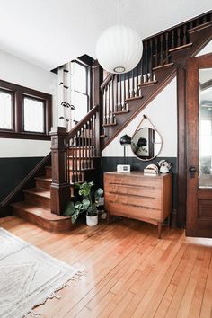 a room with a wooden floor and stairs next to a mirror on the wall near a dresser