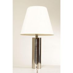 a lamp with a white shade on it sitting on a table next to a wall