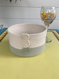 a white basket sitting on top of a yellow table next to a glass of wine