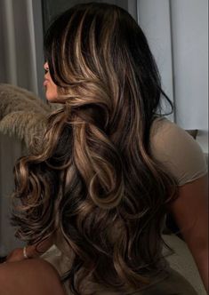 a woman with long, wavy hair sitting in front of a window looking out the window