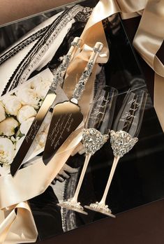 two champagne flutes sitting next to each other on top of a black table with white flowers