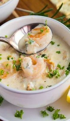 there is a bowl of soup with shrimp and lemons on the table next to bread