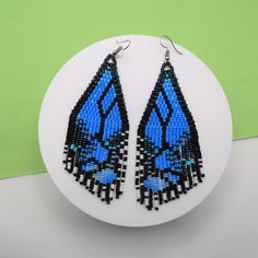 a pair of blue and black beaded earrings sitting on top of a white plate