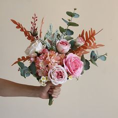 a person holding a bouquet of flowers in their hand with leaves and foliage on the side