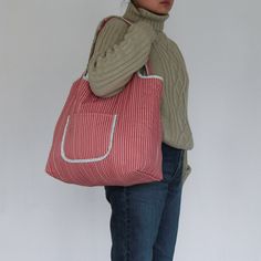 a woman holding a red and white striped handbag in front of her face while standing against a wall