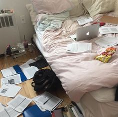 an unmade bed with papers scattered all over it and a laptop on the floor