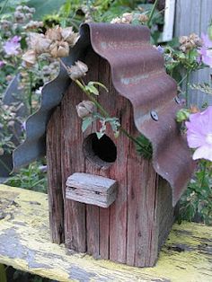 a birdhouse made out of an old wooden fence and some flowers in the background