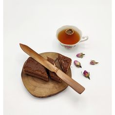 two pieces of brownie on a wooden plate next to a cup of tea