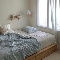 an unmade bed sitting next to a window in a room with wooden floors and white walls