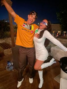 a man and woman posing for a photo on a deck at night with their arms in the air