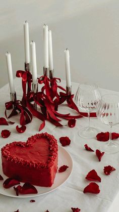 a heart shaped cake sitting on top of a table next to wine glasses and candles