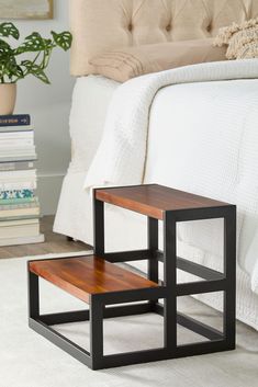 two small tables sitting on top of a white carpeted floor next to a bed