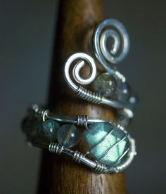 two wire wrapped rings sitting on top of a wooden stick with green and blue beads