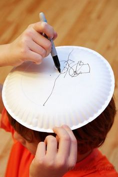 a young boy is holding a paper plate with a drawing on it and writing on it