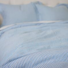 a bed with blue and white striped sheets, pillows and a cat laying on it