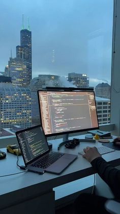 a person sitting at a desk with two laptops and a computer monitor in front of them