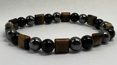 Masculine 8 mm bracelet crafted with black obsidian, Tigers's Eye, and hematite beads. The distinctive touch comes from the square tiger's eye bead separator, infusing the piece with subtle and masculine elegance. Embark on a journey of balance and well-being by combining the unique properties of obsidian, tiger's eye, and hematite. Obsidian, with its versatility, not only protects and heals but also enhances emotional and spiritual well-being, providing a valuable tool for personal growth and c Adjustable Brown Hematite Bracelet, Adjustable Hematite Brown Bracelets, Black Hematite Crystal Bracelet For Spiritual Use, Black Hematite Crystal Bracelet Spiritual, Black Hematite Spiritual Crystal Bracelet, Black Spiritual Hematite Crystal Bracelet, Handmade Black Hematite Beaded Bracelets, Adjustable Brown Hematite Beaded Bracelets, Adjustable Black Hematite Crystal Bracelet